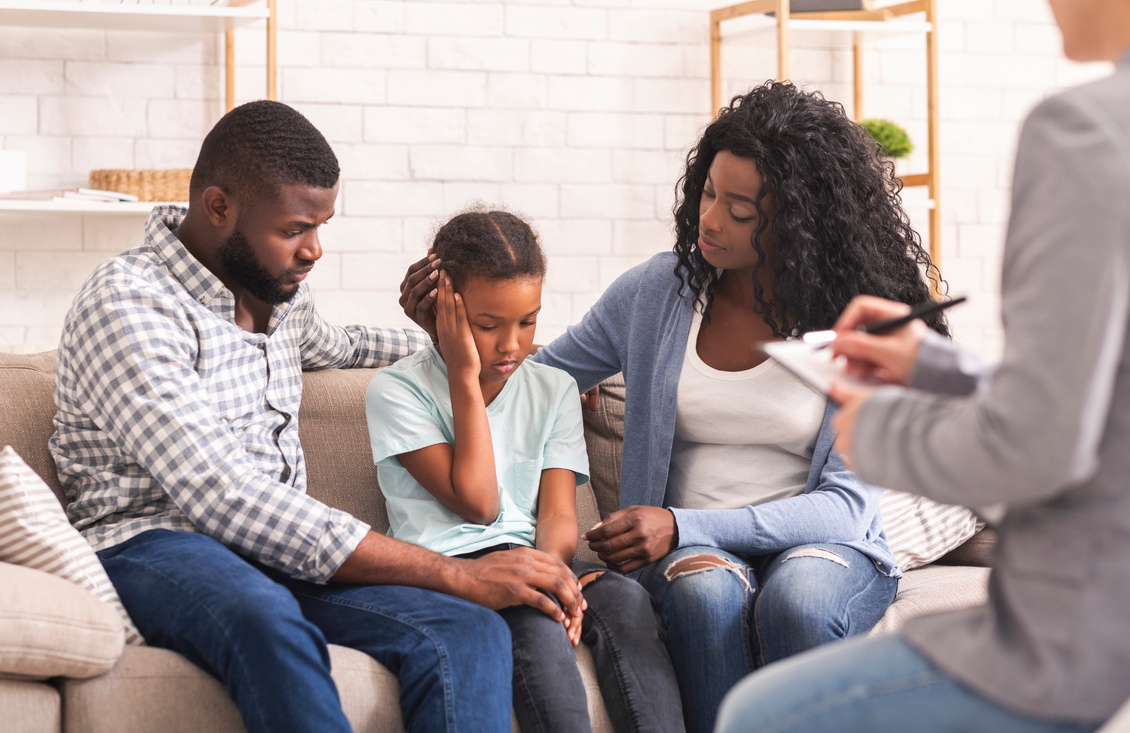 Caring black parents soothing their little daughter at psychologist consultation